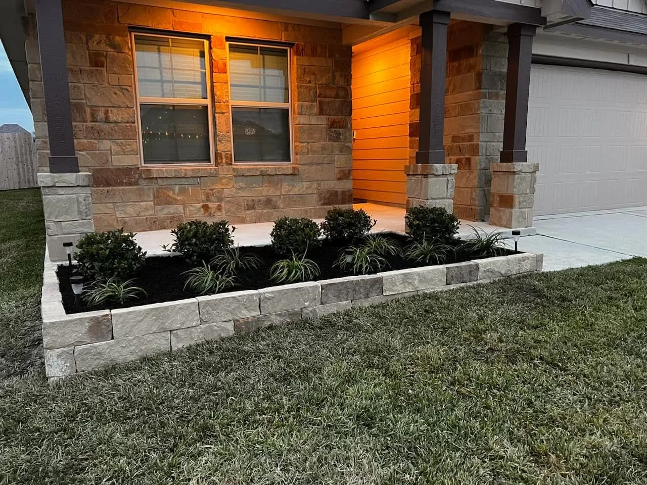 Flower bed with stacked stone border and new plantings along a front porch