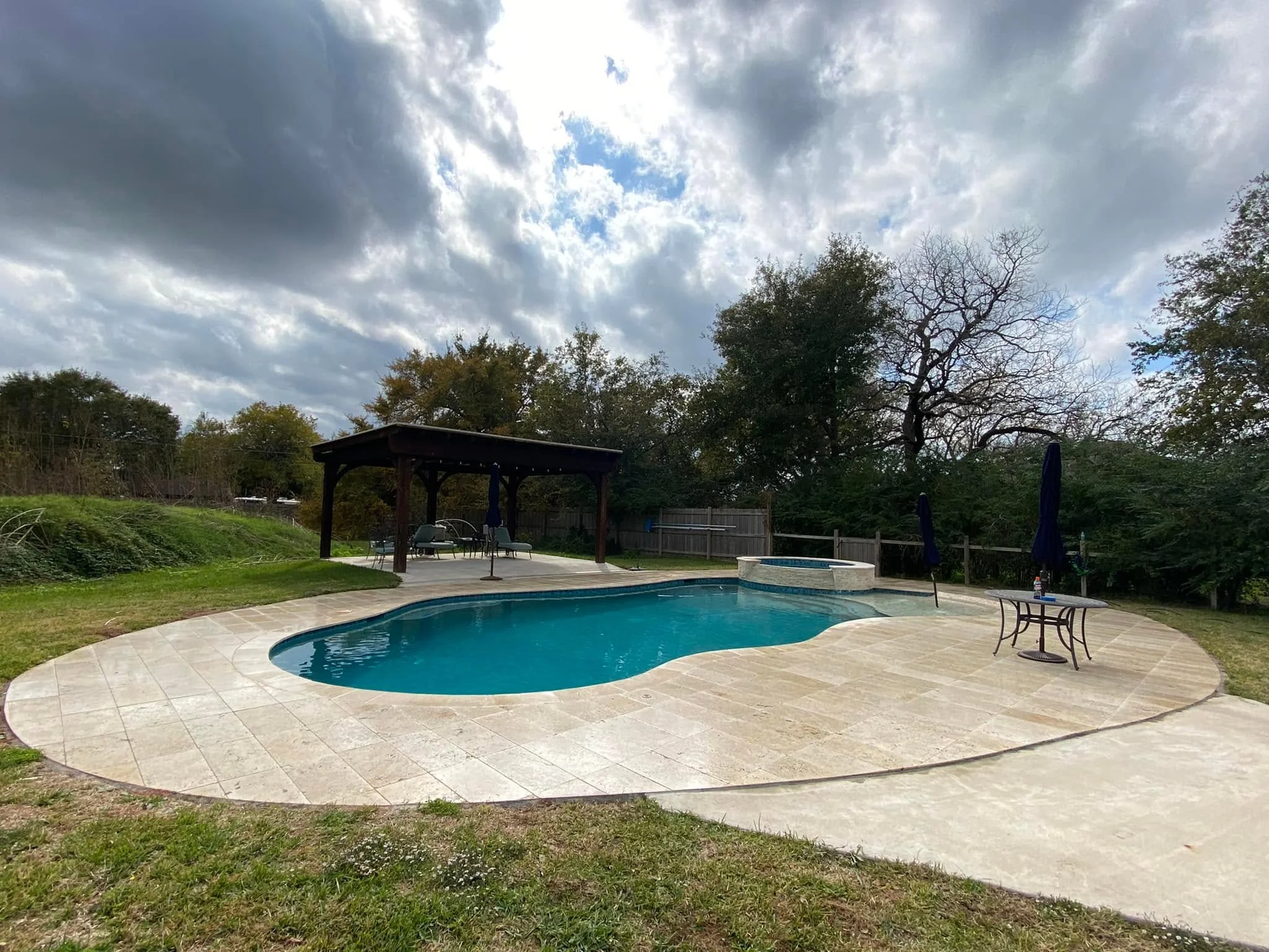 Travertine pool patio and covered pergola built by GreenRiver Landscaping in Bryan, Texas
