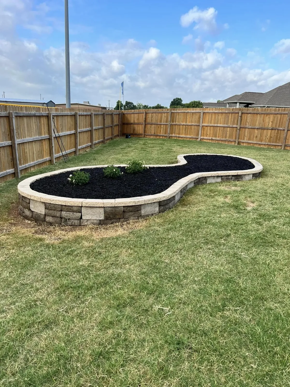 Curved block raised bed with black mulch set in a fenced lawn