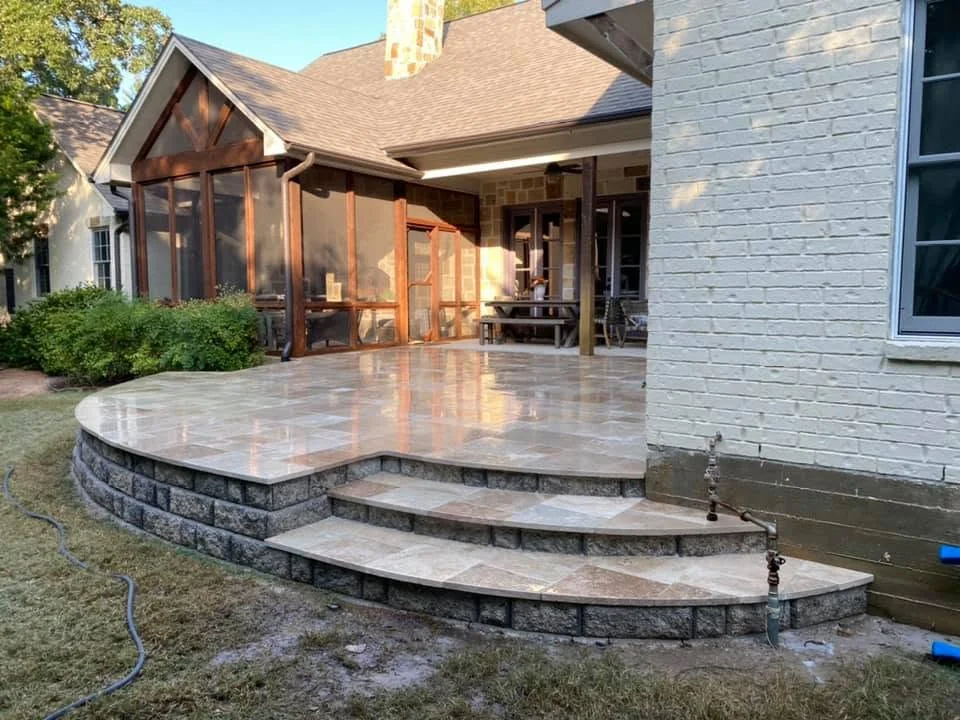 Stone patio with block steps and retaining wall behind a brick home in Bryan, Texas