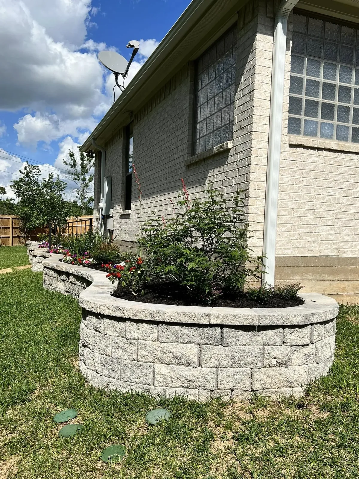 Curved stone planter wall with new shrubs beside a brick home